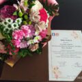 Zdjęcie przedstawia bukiet kwiatów w odcieniach różowych i białych oraz list zawierający życzenia z okazji dnia seniora.