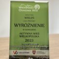 Zdjęcie przedstawia grawerton w kolorze zielonym, na którym jest napisane: "Wielkopolska odnowa wsi sołectwo Wieleń Gmina Przemęt wyróżnienie w konkursie aktywna wieś wielkopolska 2023 Krzysztof Grabowski Wicemarszałek Województwa Wielkopolskiego".