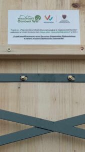 Zdjęcie przedstawia tabliczkę, na której jest napisane Projekt pn. "Poprawa stanu infrastruktury rekreacyjnej w miejscowości Barchlin" realizowany w ramach konkursu ofert "Nasza wieś, naszą wspólną sprawą" w 2023 r. "Projekt współfinansowany przez Samorząd Województwa Wielkopolskiego w ramach programu Wielkopolska Odnowa Wsi".