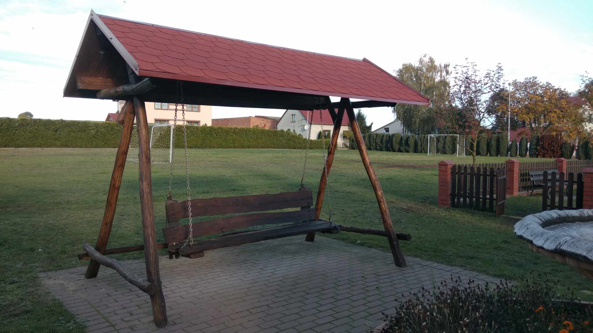 Na zdjęciu widnieje huśtawka ogrodowa z zadaszeniem.