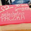 Zdjęcie przedstawia czerwony tort z napisem szlachetna paczka oraz 10-lecie Grażyny. Tort zdobi tez serce wykonane z lukru.
