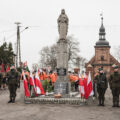 Zdjęcie przedstawia żołnierzy pełniących wartę przy pomniku na rynku. W tle orkiestra dęta.