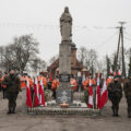 Zdjęcie przedstawia żołnierzy pełniących wartę przy pomniku na rynku. W tle orkiestra dęta.