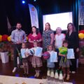 Wspólne zdjęcie laureatów z jury oraz organizatorami. Dzieci pozują z nagrodami. Wszyscy pozują na tle sceny, na której jest projektor, na którym widnieje napis: "XIII Gminny Konkurs Recytatorski Przedszkolaków". Scena ozdobiona jest kolorowymi dodatkami.