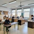 Uczestnicy siedzą w ławkach i oczekują na rozpoczęcie konkursu.