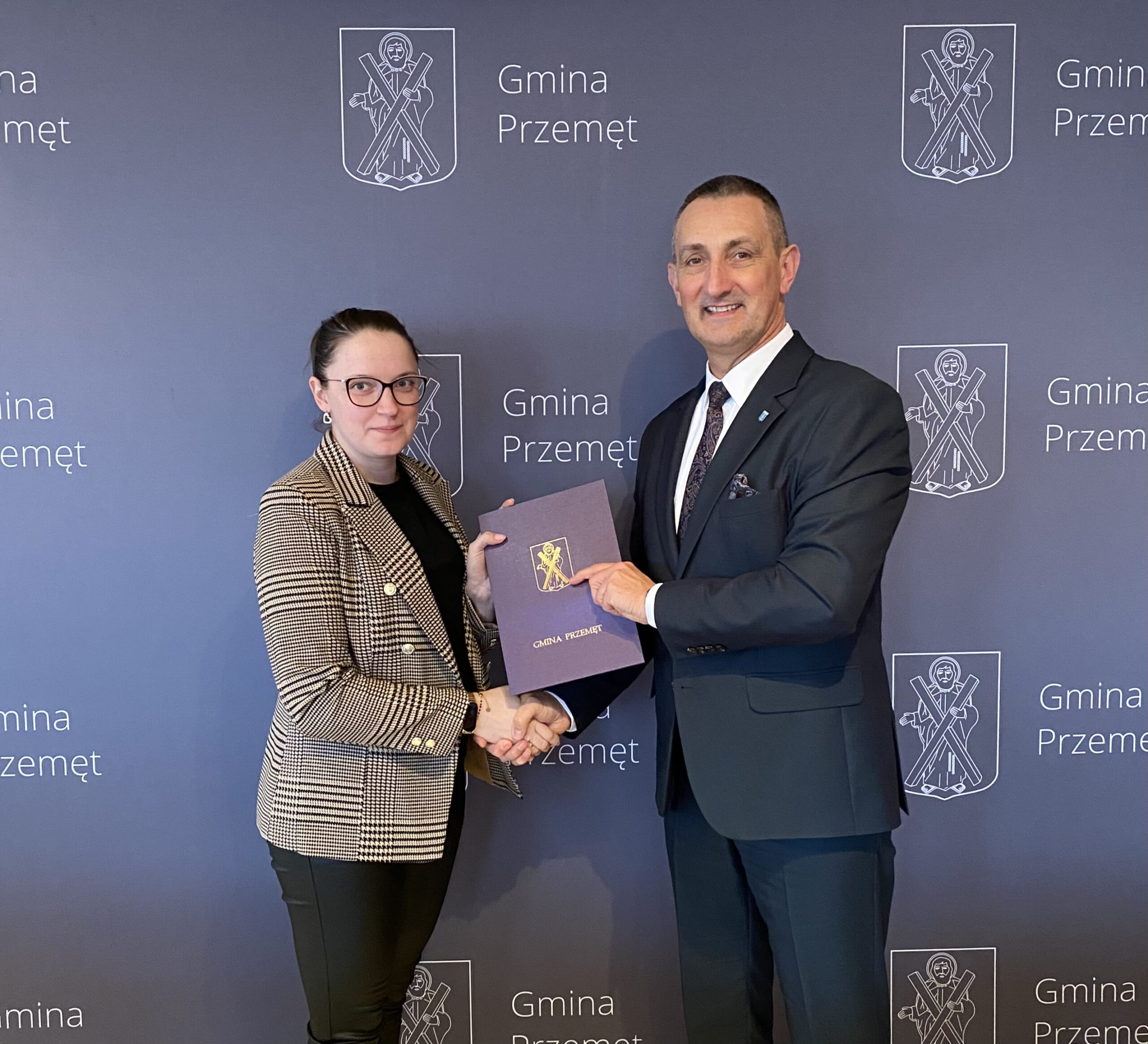 Zdjęcie przedstawia Wójta Gminy Przemęt wraz z przedstawicielem firmy brukarskiej - HC firma usługowo-handlowa Henryk Cieplik. Osoby ww. podają sobie dłoń na tle ścianki Gmina Przemęt.