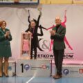 Dziewczynka z lalką na podium, obok kobieta i mężczyzna.