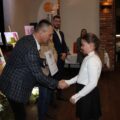 Na zdjęciu wójt wręcza uczennicy dyplom oraz składa gratulacje. W tle dyrektor GCKiB.