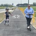 Zdjęcie przedstawia uczennicę ze szkoły w Starkowie oraz dyrektora szkoły. Dziewczynka, jedzie na rolkach, a Dyrektor szkoły na hulajnodze elektrycznej. Obie jadą ścieżką ze Starkowa zmierzając w stronę Błotnicy.