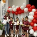 Na zdjęciu pozują przedszkolaki z Siekowa z medalami, dyplomami oraz nagrodami wraz z przedszkolanką (opiekunem drużyny) na ściance ozdobionej balonami w barwach białych i czerwonych. Obok ścianki winder Honorowy Patronat Wójta Gminy Przemęt.