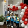 Na zdjęciu pozują przedszkolaki z Bucza "0" z medalami, dyplomami oraz nagrodami wraz z przedszkolanką (opiekunem drużyny) na ściance ozdobionej balonami w barwach białych i czerwonych. Obok ścianki winder Honorowy Patronat Wójta Gminy Przemęt.