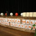 Na zdjęciu scena w Gminnym Centrum Kultury i Biblioteki w Przemęcie. Z przodu sceny widnieje napis drukowanymi literami PRZEMĘT - NASZA MAŁA, ZDROWA OJCZYZNA. Oprócz tego na scenie widoczne są balony w kolorach białych i czerwonych oraz podziękowania dla gości w postaci drewnianych statuetek.