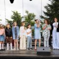 Dzieci stoją na scenie i śpiewają przez mikrofony.