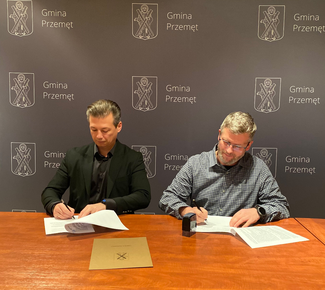 Na zdjęciu zastępca wójta gminy Przemęt Waldemar Kalitka wraz z właścicielem firmy PHU plus MINUS Robertem Dydyną. Wyżej wymienieni podpisują umowę. W tle ścianka z herbem gminy Przemęt.