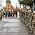 Na zdjęciu żołnierze z 5 Lubuskiego Pułku ustawieni w rzędzie na rynku. W tle poczty sztandarowe.