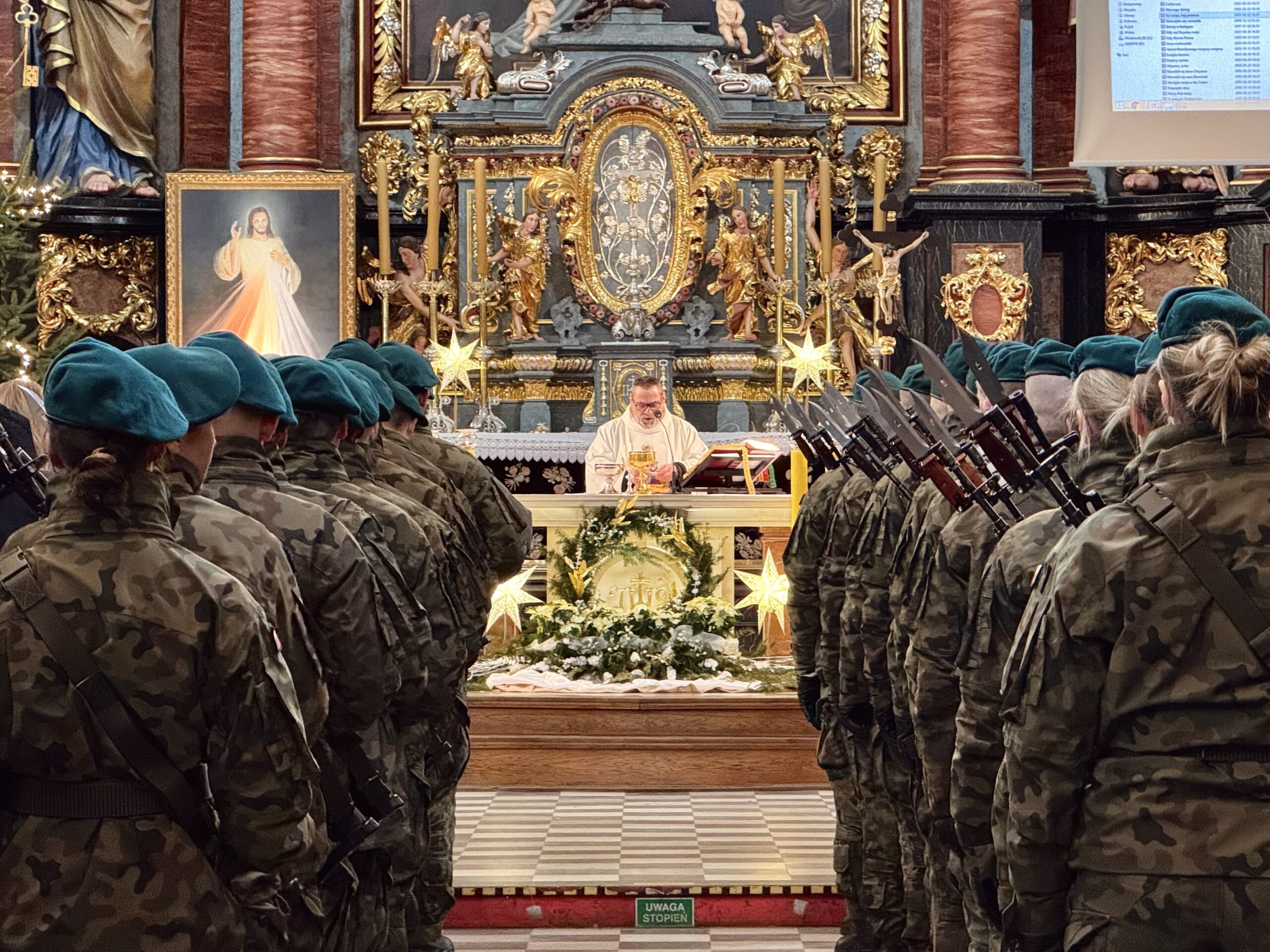 Na zdjęciu żołnierze ustawieni w dwóch rzędach wzdłuż korytarza w kościele. Na fotografii widać także ołtarz oraz księdza proboszcza podczas odprawiania mszy świętej.
