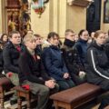 Zdjęcie przedstawia osoby siedzące w ławkach podczas mszy świętej.