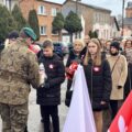 Na zdjęciu żołnierz odbiera znicz od delegacji składające się z trójki uczniów szkoły.