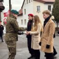 Na zdjęciu żołnierz odbiera znicz od delegacji składające się z trójki uczniów szkoły.