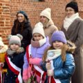 Na zdjęciu czwórka dziewczynek i trzy dorosłe kobiety. Trójka dziewczynek trzyma róże i mają ubrane biało-czerwone szarfy.