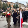 Na zdjęciu żołnierz składa, odebraną od delegacji, wiązankę kwiatów pod pomnikiem na rynku. W tle delegacje.