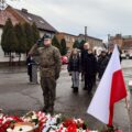 Na zdjęciu żołnierz salutuje przed pomnikiem. W tle delegacje.