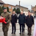 Na zdjęciu żołnierz składa, odebraną od delegacji, wiązankę kwiatów pod pomnikiem na rynku. W tle delegacje.