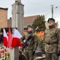 Na zdjęciu dwójka żołnierzy stoi koło pomnika na rynku.
