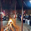 Na zdjęciu osoby obecne na uroczystości w wigwamie. Na fotografii widoczne także palące się ognisko.