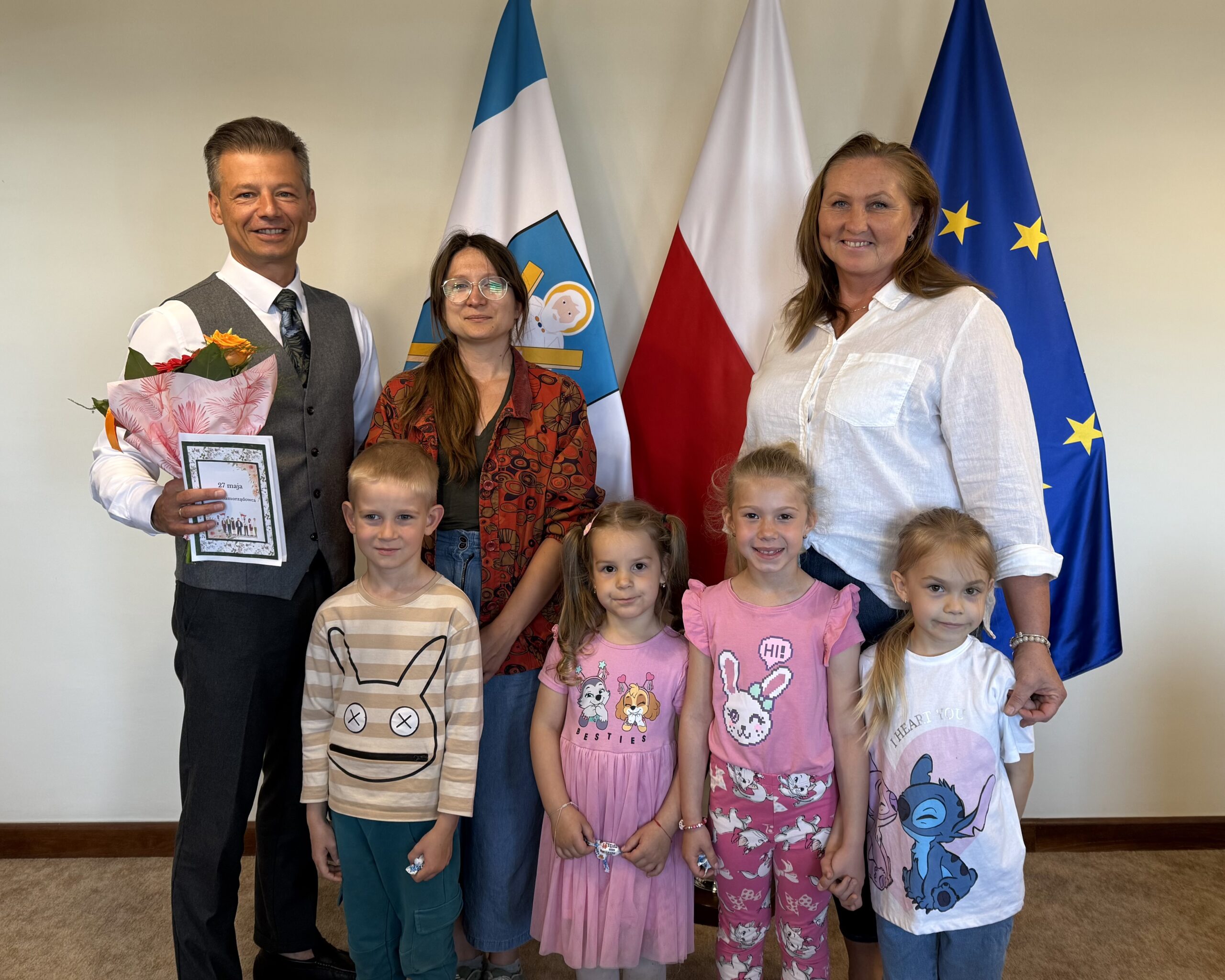 Wspólne zdjęcie zastępcy wójta z trójką przedszkolaków i dyrektorką przedszkola. Zastępca trzyma w ręce kwiaty i laurkę.