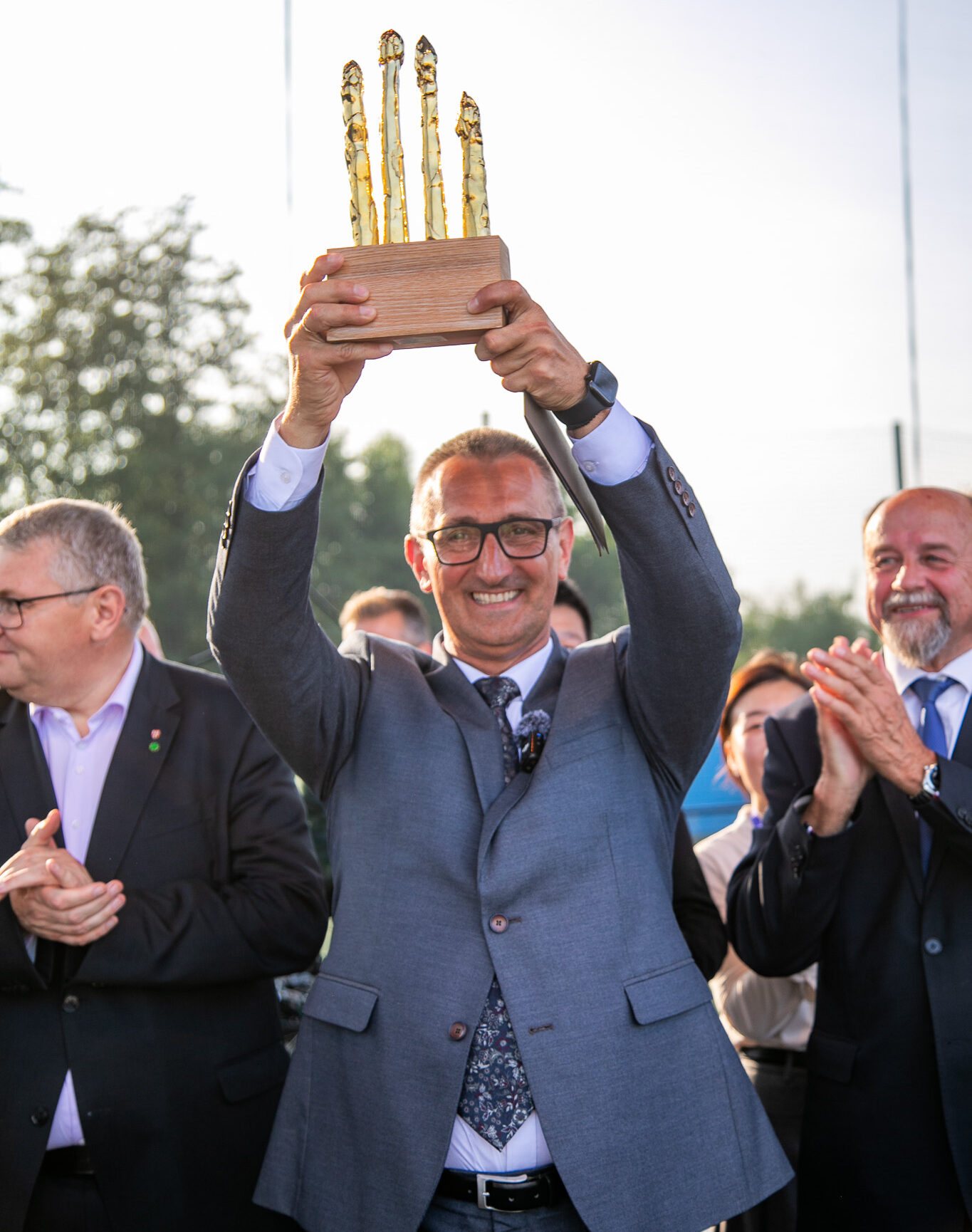 Na fotografii wójt Janusz Frąckowiak, który trzyma w górze statuetkę złotych szparagów. W tle inne osoby bijące brawo.