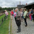 Na fotografii widoczni seniorzy podczas zwiedzania. Na zdjęciu widać także leżące zwierzęta za ogrodzeniem.