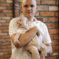 Na zdjęciu widzimy ojca trzymającego niemowlę w ramionach.