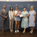 Na zdjęciu uczestnicy gali noworodkowej. Na tle oficjalnej ścianki z herbem gminy stoi mama z niemowlęciem. Kobieta pozuje z listem gratulacyjnym i upominkiem. Na fotografii Wójt Gminy Przemęt Janusz Frąckowiak, Przewodnicząca Rady Gminy Monika Maćkowiak, Zastępca Kierownika Urzędu Stanu Cywilnego Irena Mikołajczak i pracownik urzędu pani Natalia Chomska.