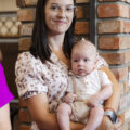 Na zdjęciu widzimy mamę trzymającą niemowlę w ramionach.