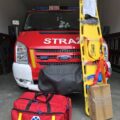 Na fotografii nowoczesny zestaw ratownictwa przedlekarskiego na bazie standardu R1 wraz z deską ortopedyczną. W tle wóz strażacki.