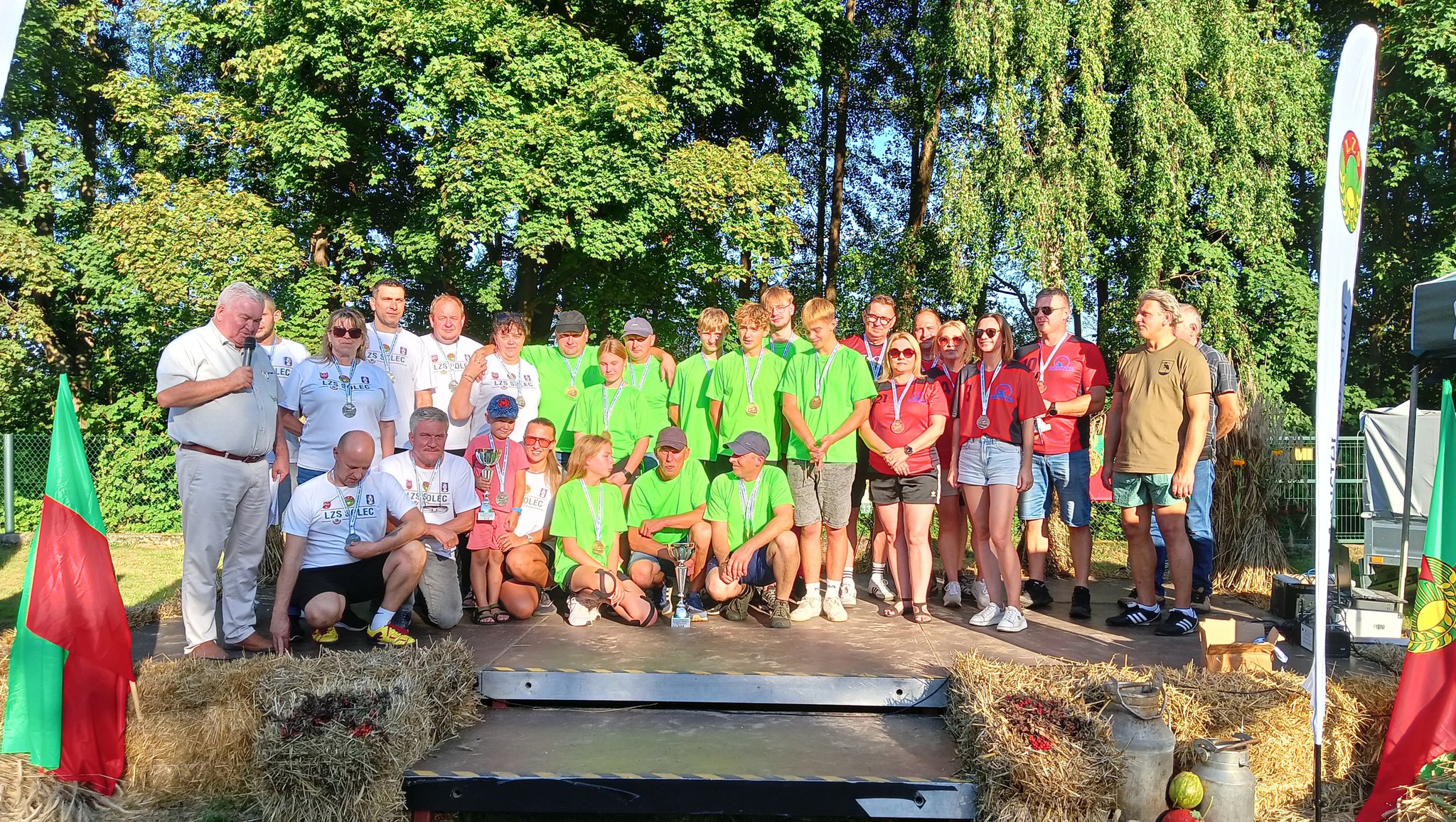 Grupowe zdjęcie zwycięskich drużyn wraz z panem Krzysztofem Piaskiem. Osoby pozują z medalami i pucharami.