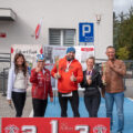 Na zdjęciu widoczni uczestnicy po zakończonym biegu. Pozują z medalami i pucharem. Na fotografii obecny jest także wójt. Przed nimi znajduje się sportowe podium.