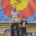 Mężczyzna oraz dziecko pozują do zdjęcia ze statuetkami i medalami.