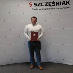 Na fotografii prezes jednostki OSP Bucz, Robert Pawłowski. Pozuje on z teczką gminy Przemęt, w której znajduje się podpisana umowa, na tle ścianki z nazwą firmy.
