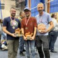 Trzech mężczyzn pozuje do zdjęcia ze statuetkami i medalami.