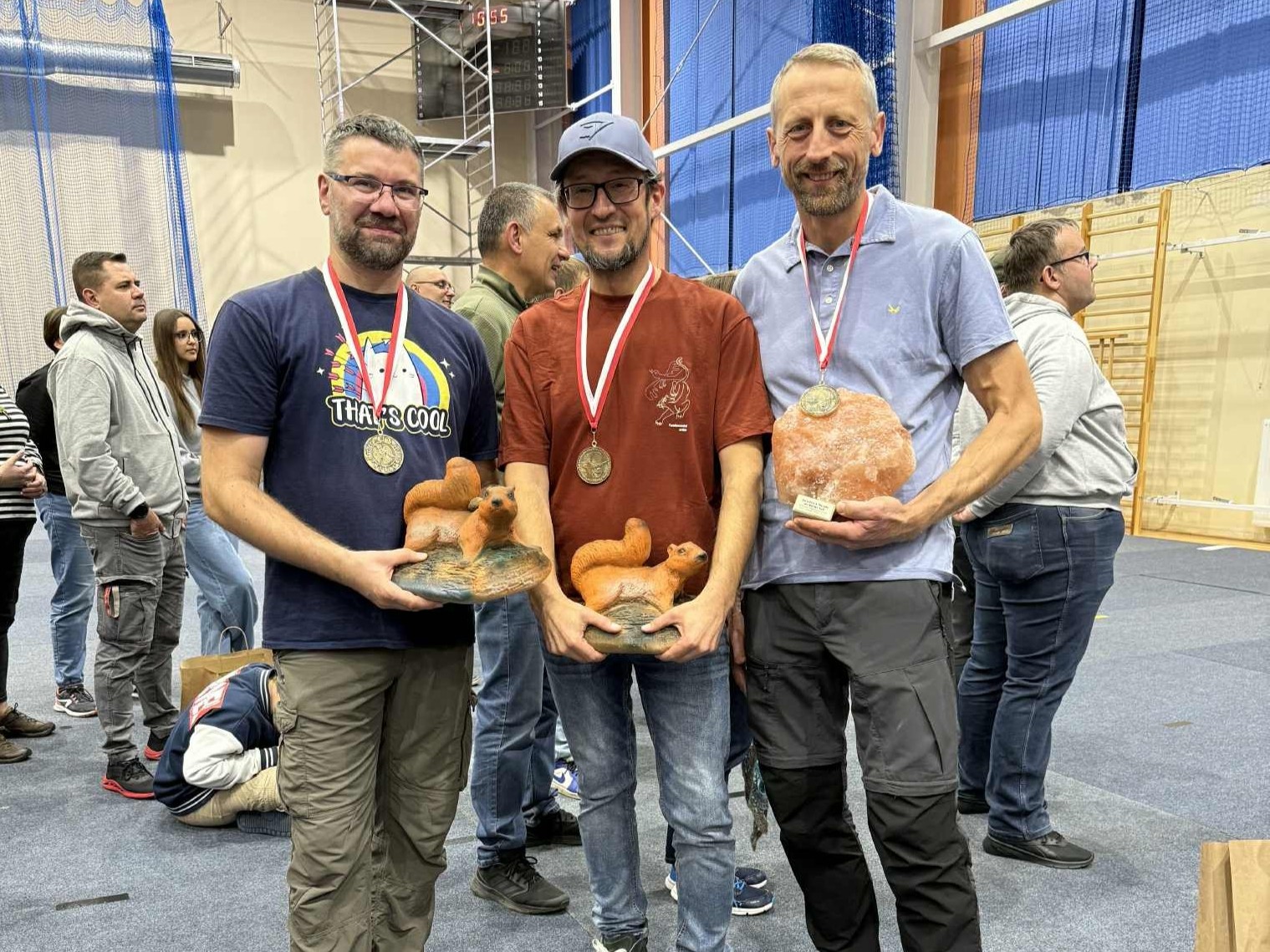 Trzech mężczyzn pozuje do zdjęcia ze statuetkami i medalami.