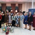 Grupowe zdjęcie osób obecnych na uroczystości. Na fotografii widać także kwiaty i upominki.