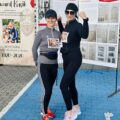Dwie uśmiechnięte kobiety pozujące do zdjęcia. Ubrane są w sportowe stroje i oznaczone numerami startowymi.