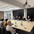 Na fotografii osoby uczestniczące w szkoleniu siedzą przy stole i słuchają szkolenia.