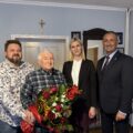 Wspólne zdjęcie, na którym znajdują się wójt, zastępca kierownika USC oraz jubilat z synem. Jubilat pozuje z bukietem kwiatów.