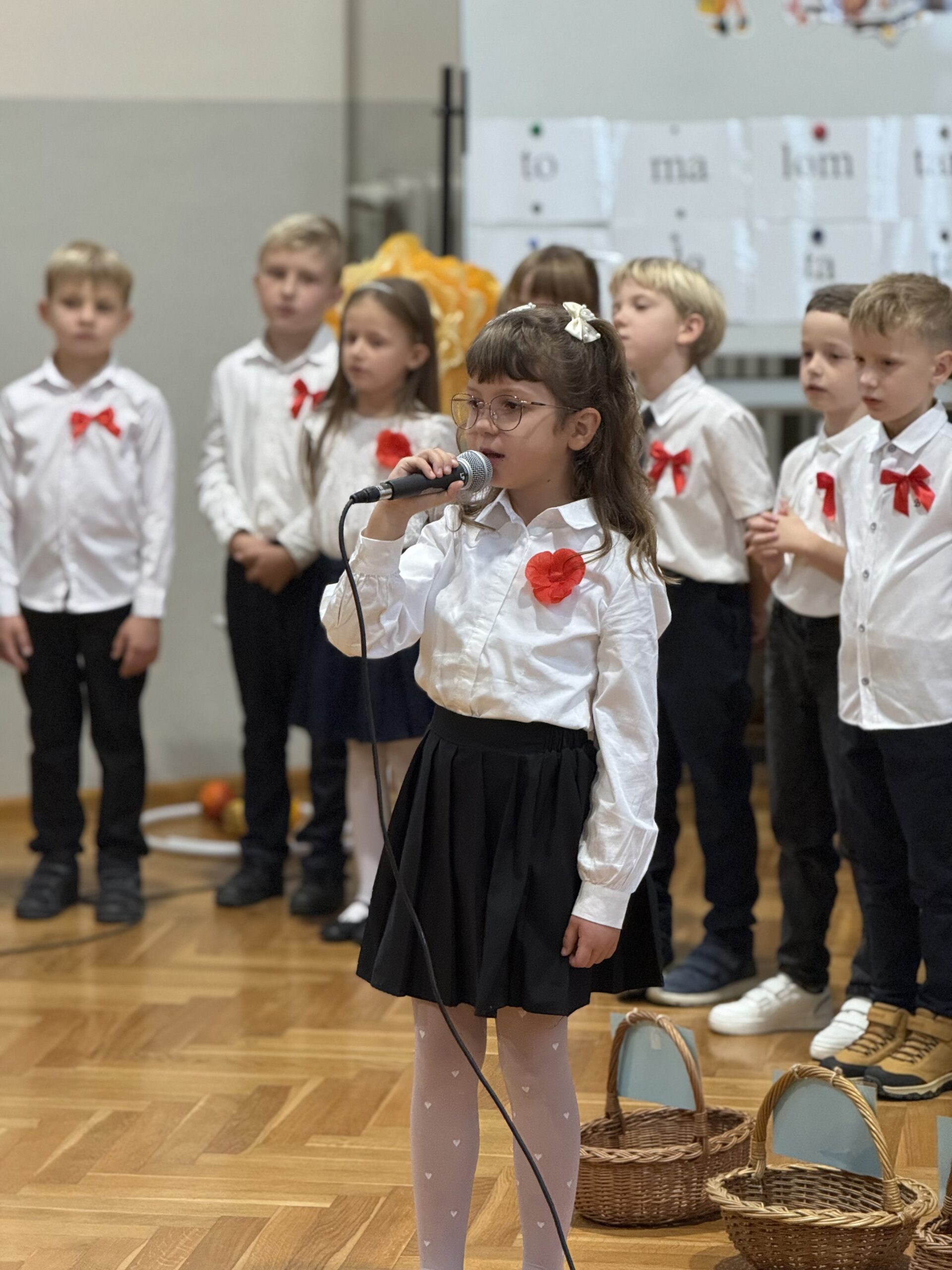 Na zdjęciu uczennica podczas występu artystycznego. W tle inni uczniowie.
