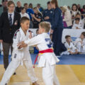 Na zdjęciu dwóch zawodników podczas sportowego pojedynku. W tle sędzia oraz widownia.