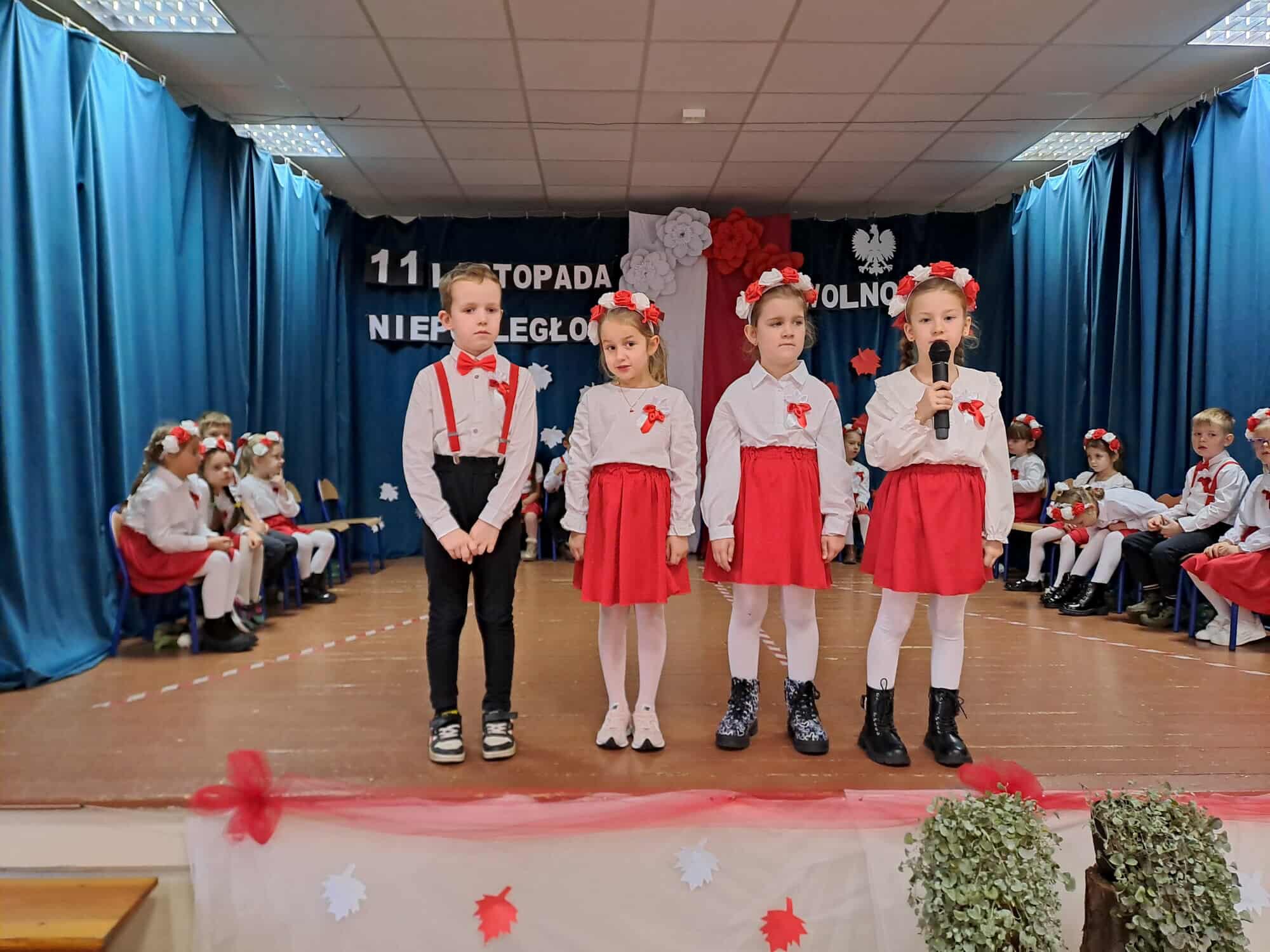 Na zdjęciu czwórka dzieci podczas występu artystycznego. W tle inne dzieci.