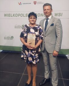 Na zdjęciu Zastępca Wójta gminy Przemęt Waldemar Kalitka oraz sołtys Kaszczoru Beata Binkowska, która pozuje ze statuetką. W tle ścianka Wielkopolska Odnowa Wsi.